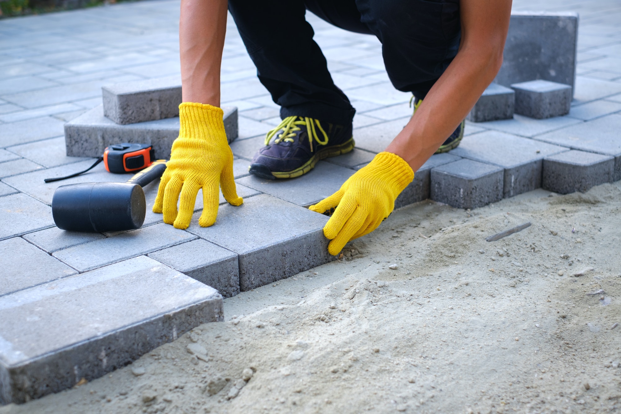 The master in yellow gloves lays paving stones